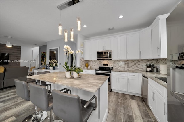 kitchen with a center island, stainless steel appliances, white cabinetry, and light hardwood / wood-style flooring