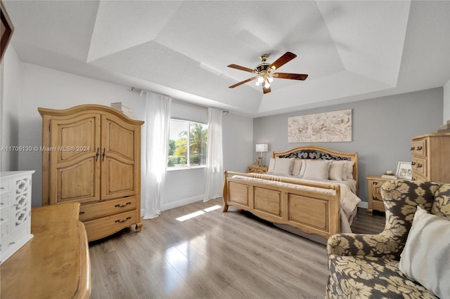 bedroom with ceiling fan, light hardwood / wood-style floors, and a raised ceiling