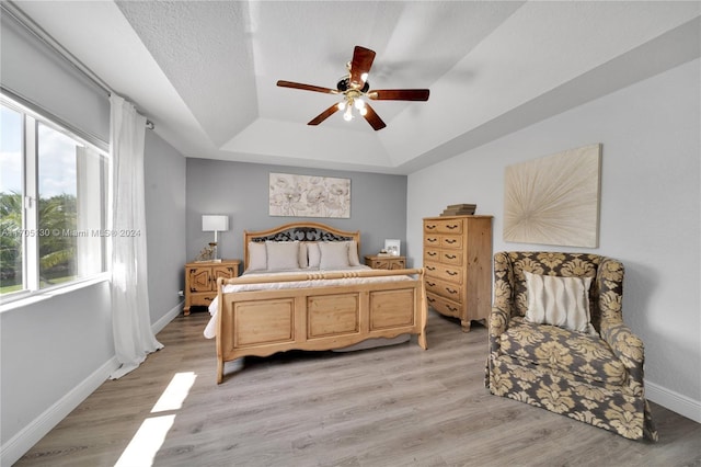 bedroom featuring ceiling fan, light hardwood / wood-style floors, a textured ceiling, and a tray ceiling