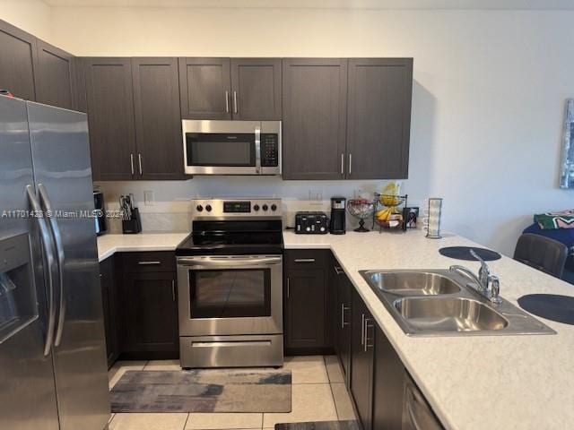 kitchen featuring dark brown cabinetry, sink, stainless steel appliances, kitchen peninsula, and light tile patterned floors