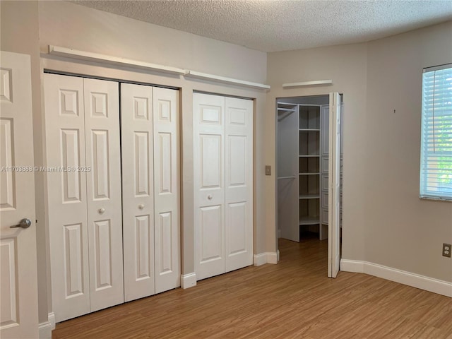 unfurnished bedroom with multiple closets, light hardwood / wood-style flooring, and a textured ceiling