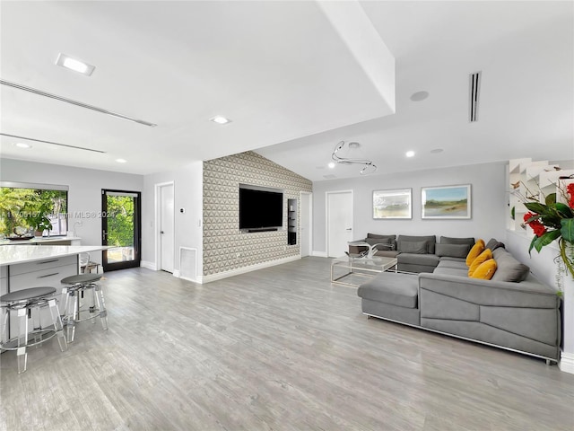 living room with baseboards, vaulted ceiling, light wood-type flooring, and visible vents