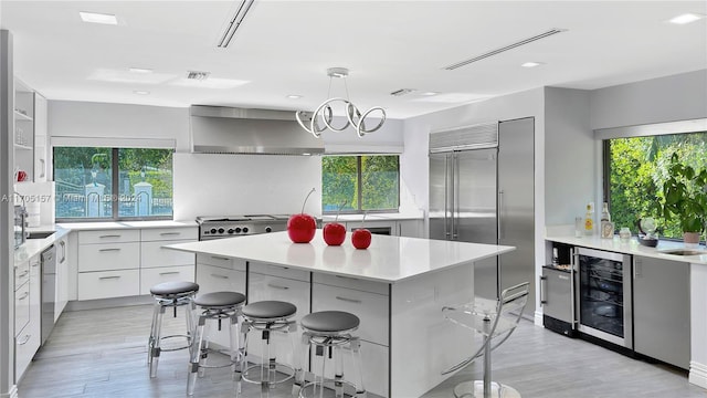 kitchen with wall chimney range hood, light countertops, beverage cooler, a kitchen island, and modern cabinets