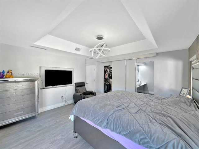 bedroom with visible vents, wood finished floors, baseboards, a chandelier, and a tray ceiling