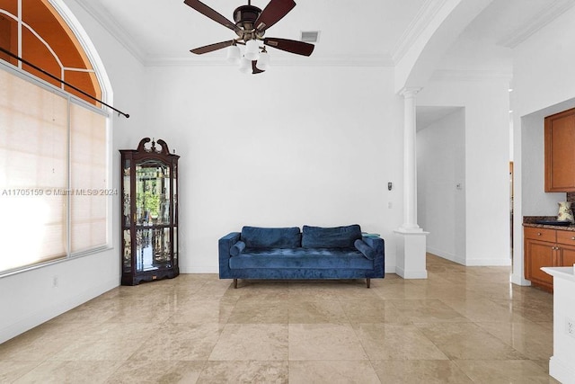 living area featuring decorative columns, crown molding, and ceiling fan