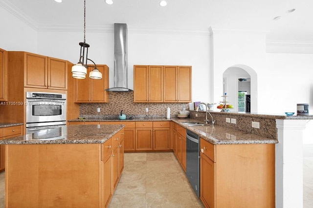 kitchen with sink, wall chimney range hood, kitchen peninsula, pendant lighting, and appliances with stainless steel finishes