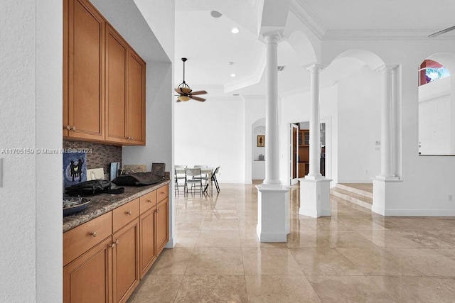 kitchen with ornate columns, ceiling fan, backsplash, dark stone countertops, and crown molding