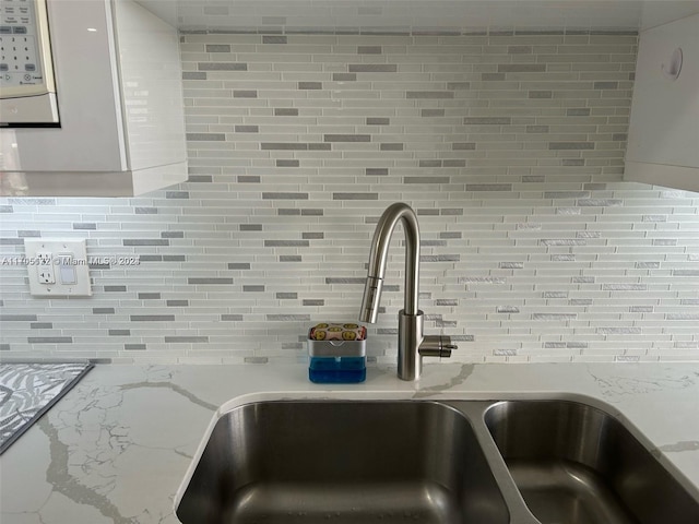 room details with backsplash, light stone counters, white cabinetry, and sink