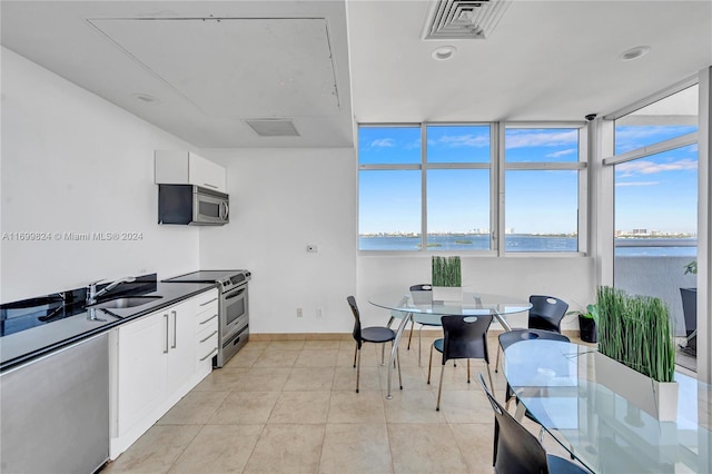 kitchen with stainless steel appliances, sink, a water view, white cabinets, and light tile patterned flooring