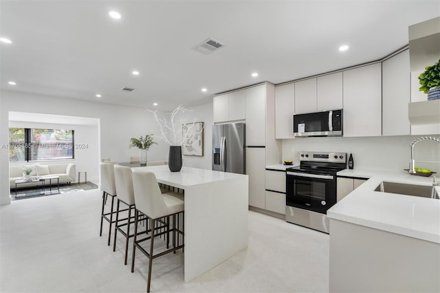 kitchen with white cabinets, sink, a breakfast bar area, a kitchen island, and stainless steel appliances