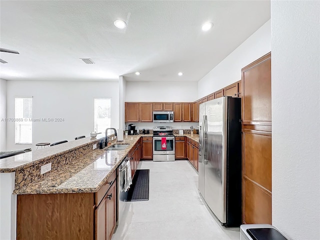 kitchen featuring kitchen peninsula, appliances with stainless steel finishes, light stone countertops, a textured ceiling, and sink