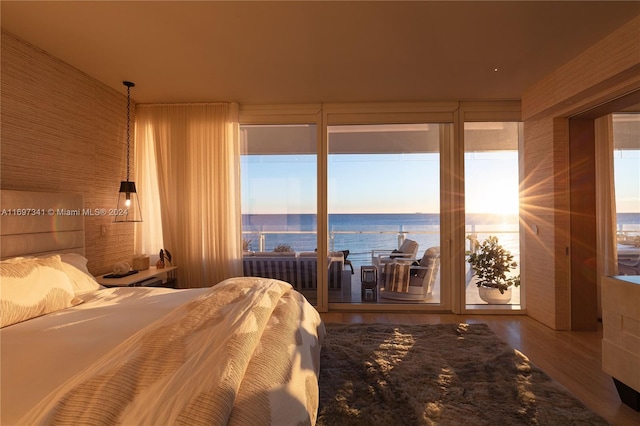 bedroom with hardwood / wood-style floors, a water view, and access to outside