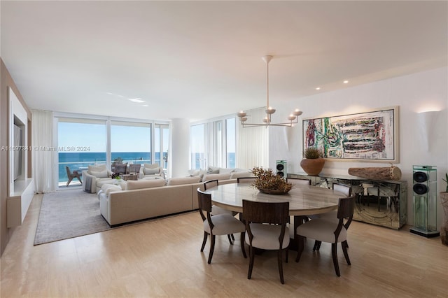 dining area featuring light wood-type flooring, a water view, floor to ceiling windows, and a notable chandelier