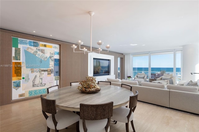 dining space with a notable chandelier, a water view, a wall of windows, and light hardwood / wood-style flooring