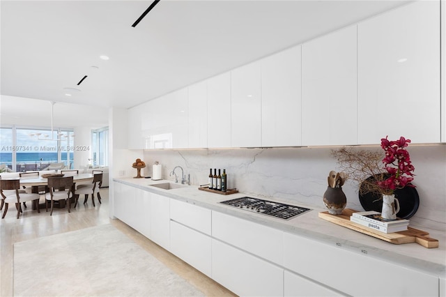 kitchen with light wood-type flooring, tasteful backsplash, sink, white cabinets, and stainless steel gas stovetop