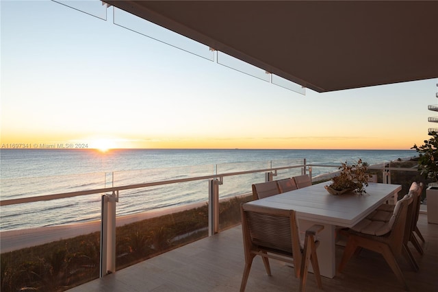 balcony at dusk featuring a beach view and a water view