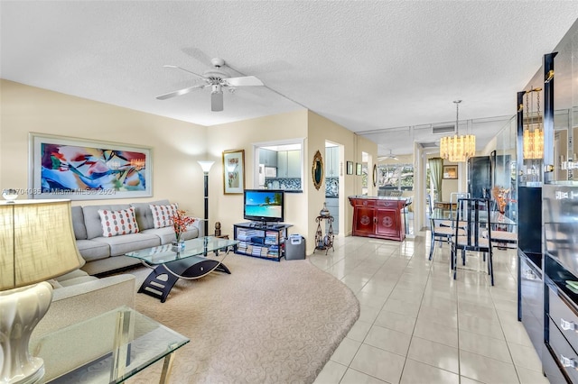 living room featuring ceiling fan with notable chandelier, light tile patterned floors, and a textured ceiling