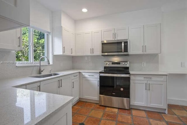 kitchen with dark tile patterned flooring, sink, light stone countertops, appliances with stainless steel finishes, and white cabinetry