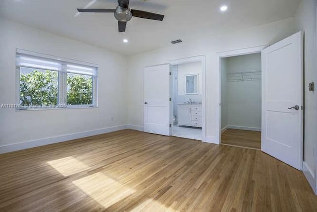 unfurnished bedroom with ensuite bath, ceiling fan, a closet, and wood-type flooring