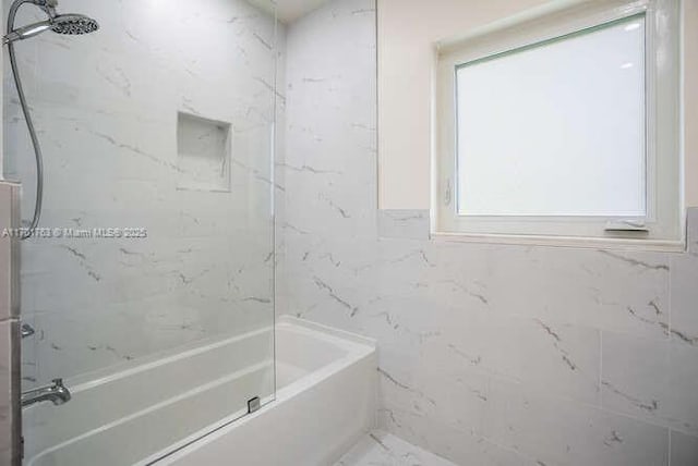 bathroom with a healthy amount of sunlight, tiled shower / bath, and tile walls