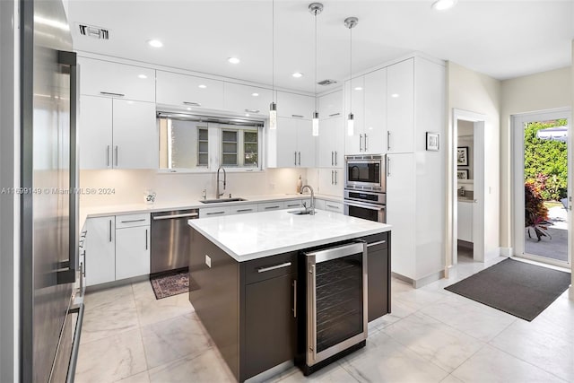 kitchen with stainless steel appliances, a kitchen island with sink, sink, decorative light fixtures, and wine cooler