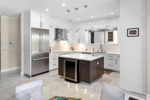 kitchen featuring beverage cooler, built in fridge, stovetop, an island with sink, and decorative light fixtures