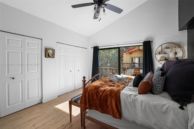 bedroom featuring high vaulted ceiling, ceiling fan, light wood-type flooring, a textured ceiling, and multiple closets