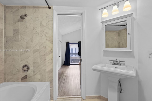 bathroom with tiled shower / bath combo, hardwood / wood-style flooring, lofted ceiling, and sink