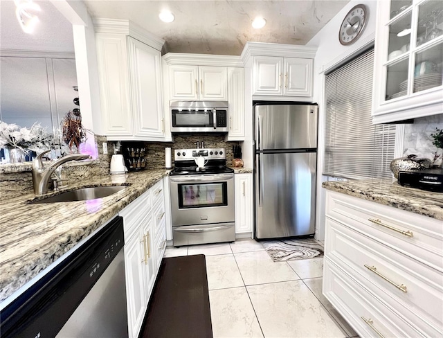 kitchen with sink, appliances with stainless steel finishes, tasteful backsplash, light stone counters, and white cabinetry