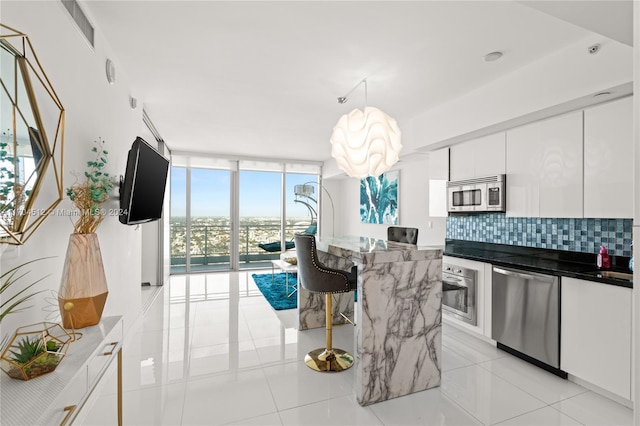 kitchen featuring floor to ceiling windows, tasteful backsplash, decorative light fixtures, white cabinetry, and stainless steel appliances