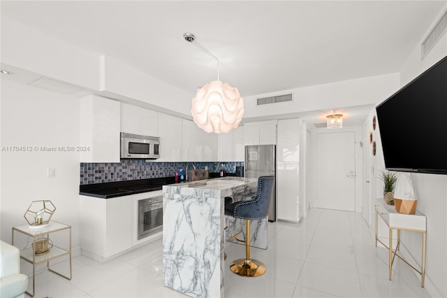 kitchen with decorative backsplash, appliances with stainless steel finishes, white cabinetry, hanging light fixtures, and light tile patterned flooring