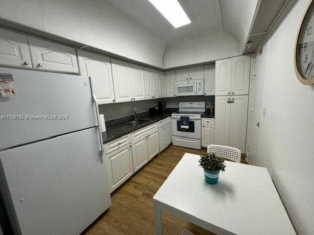 kitchen featuring white appliances, vaulted ceiling, sink, white cabinets, and dark hardwood / wood-style floors