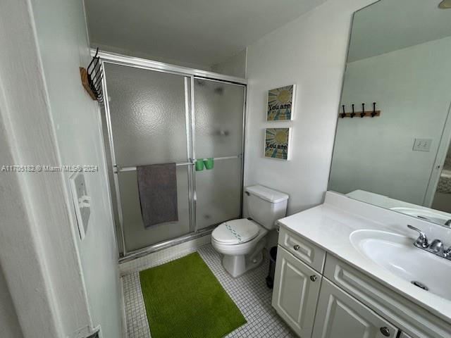 bathroom featuring toilet, vanity, tile patterned floors, and an enclosed shower