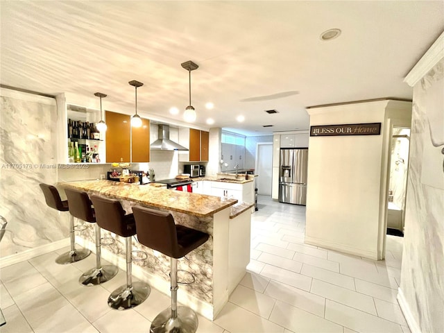 kitchen featuring kitchen peninsula, hanging light fixtures, a breakfast bar area, stainless steel appliances, and wall chimney exhaust hood