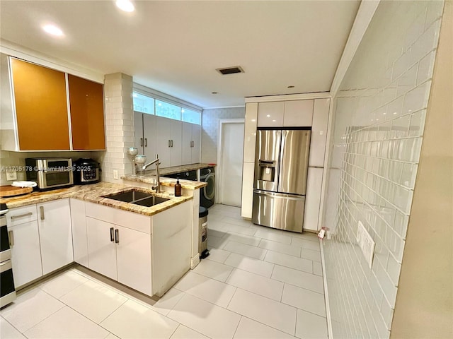 kitchen featuring tile walls, stainless steel refrigerator with ice dispenser, sink, light tile patterned floors, and white cabinets