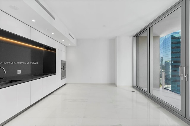 interior space with backsplash, white cabinetry, a sink, modern cabinets, and baseboards