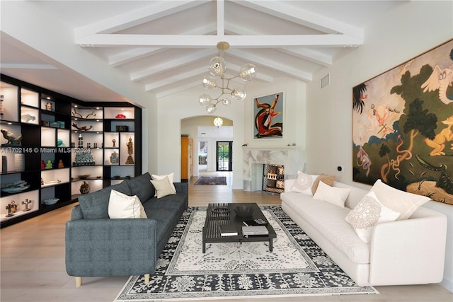 living room with lofted ceiling with beams, built in shelves, a premium fireplace, light hardwood / wood-style floors, and a chandelier