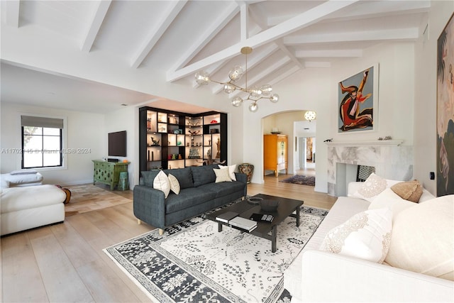 living room with lofted ceiling with beams, light hardwood / wood-style floors, a high end fireplace, and an inviting chandelier