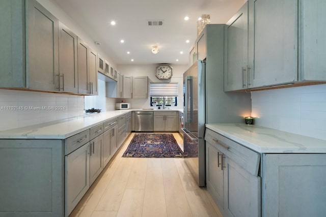 kitchen with gray cabinetry, light stone countertops, sink, stainless steel appliances, and light hardwood / wood-style flooring