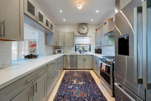 kitchen with gray cabinetry, light stone countertops, kitchen peninsula, decorative backsplash, and appliances with stainless steel finishes