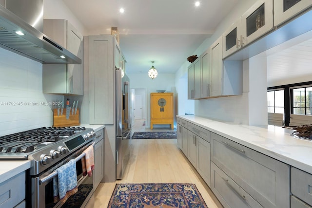 kitchen featuring appliances with stainless steel finishes, light wood-type flooring, wall chimney exhaust hood, gray cabinets, and hanging light fixtures