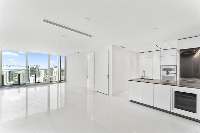 kitchen featuring sink, stainless steel double oven, beverage cooler, expansive windows, and white cabinets