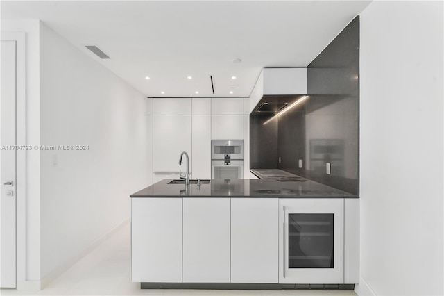 kitchen with stainless steel microwave, black electric stovetop, sink, wine cooler, and white cabinetry