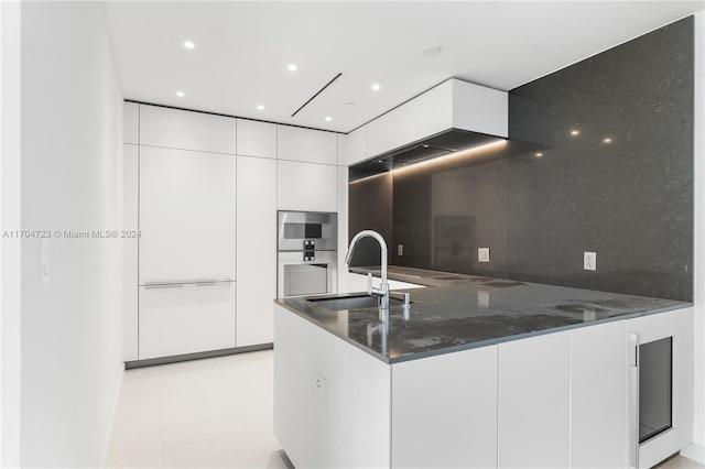 kitchen with white cabinetry, sink, backsplash, kitchen peninsula, and dark stone counters