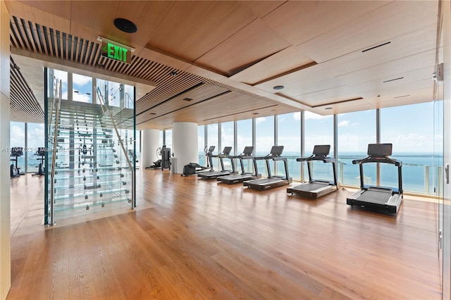 workout area with wooden ceiling, a water view, a wall of windows, and light hardwood / wood-style flooring