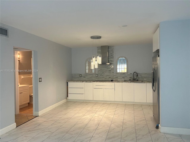 kitchen featuring decorative backsplash, black cooktop, sink, wall chimney range hood, and white cabinets