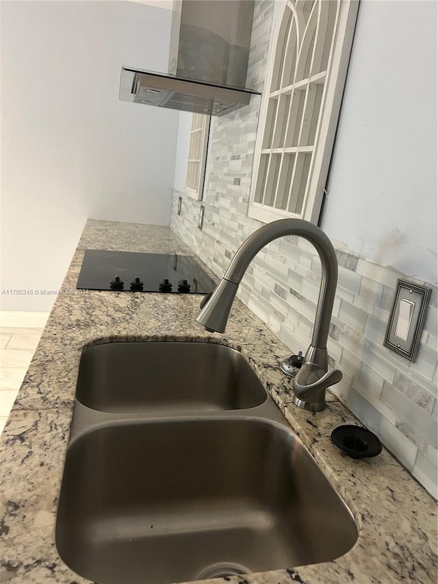 interior details with exhaust hood, black electric stovetop, sink, decorative backsplash, and light stone countertops