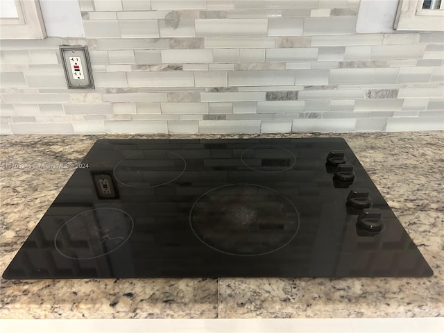 interior details with backsplash, white cabinetry, black cooktop, and light stone counters