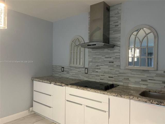 kitchen featuring wall chimney exhaust hood, black cooktop, dark stone counters, decorative backsplash, and white cabinets