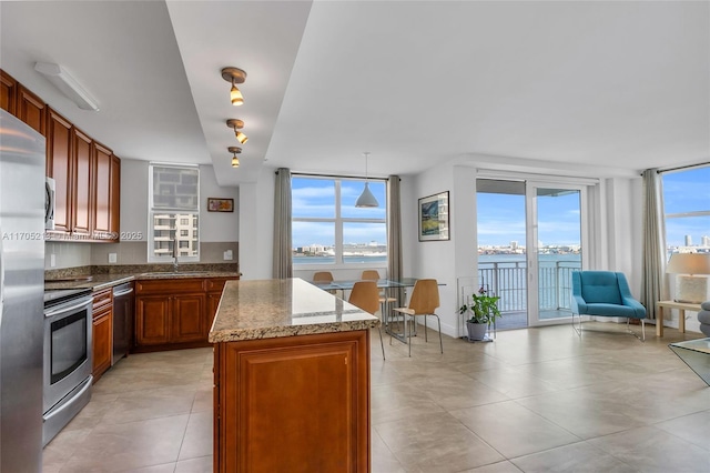 kitchen with light stone countertops, stainless steel appliances, a sink, a center island, and brown cabinetry